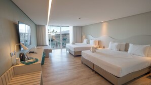 Habitación de hotel con dos camas, un escritorio con lámpara, una silla y un balcón con vistas.