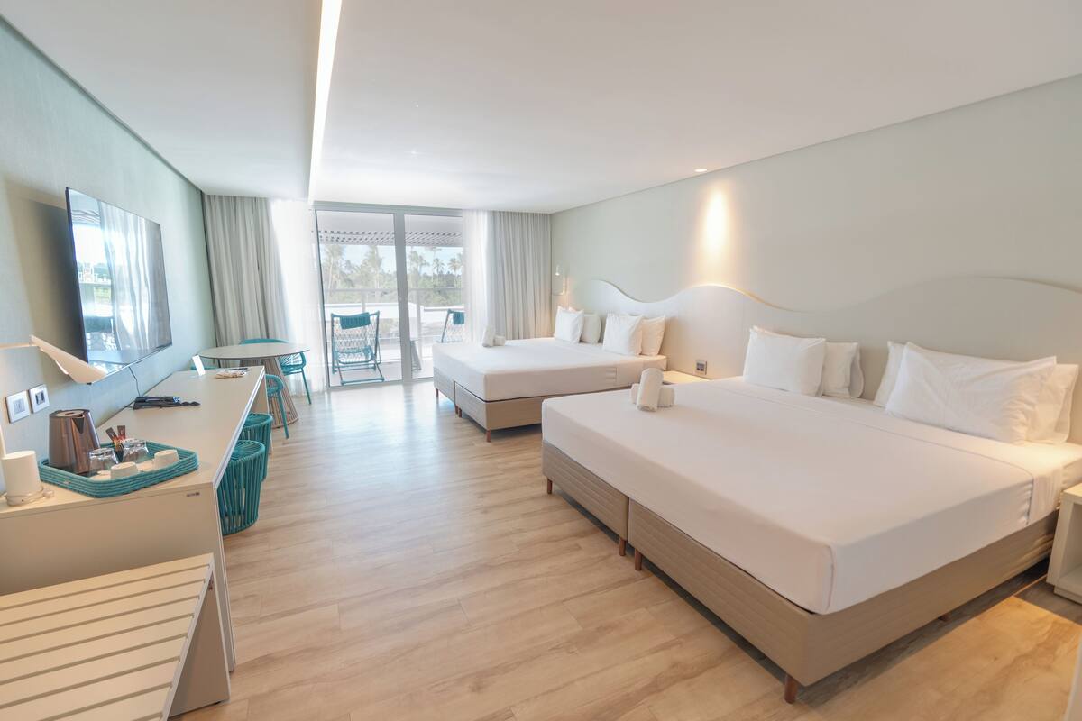 Een hotelkamer met twee bedden, een bureau, een stoel en een balkon met uitzicht.