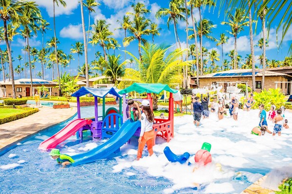 Un área de juegos acuáticos con toboganes y piscina, rodeado de palmeras y edificios.