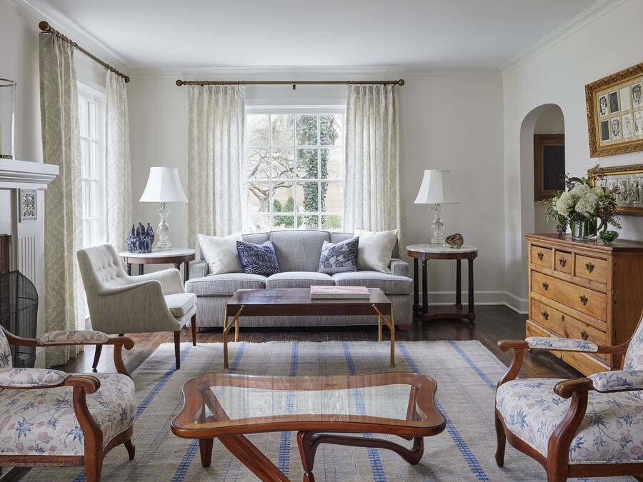 Un salon comprenant un canapé, des fauteuils, une table basse, une cheminée et une commode ornée de cadres avec des photos.