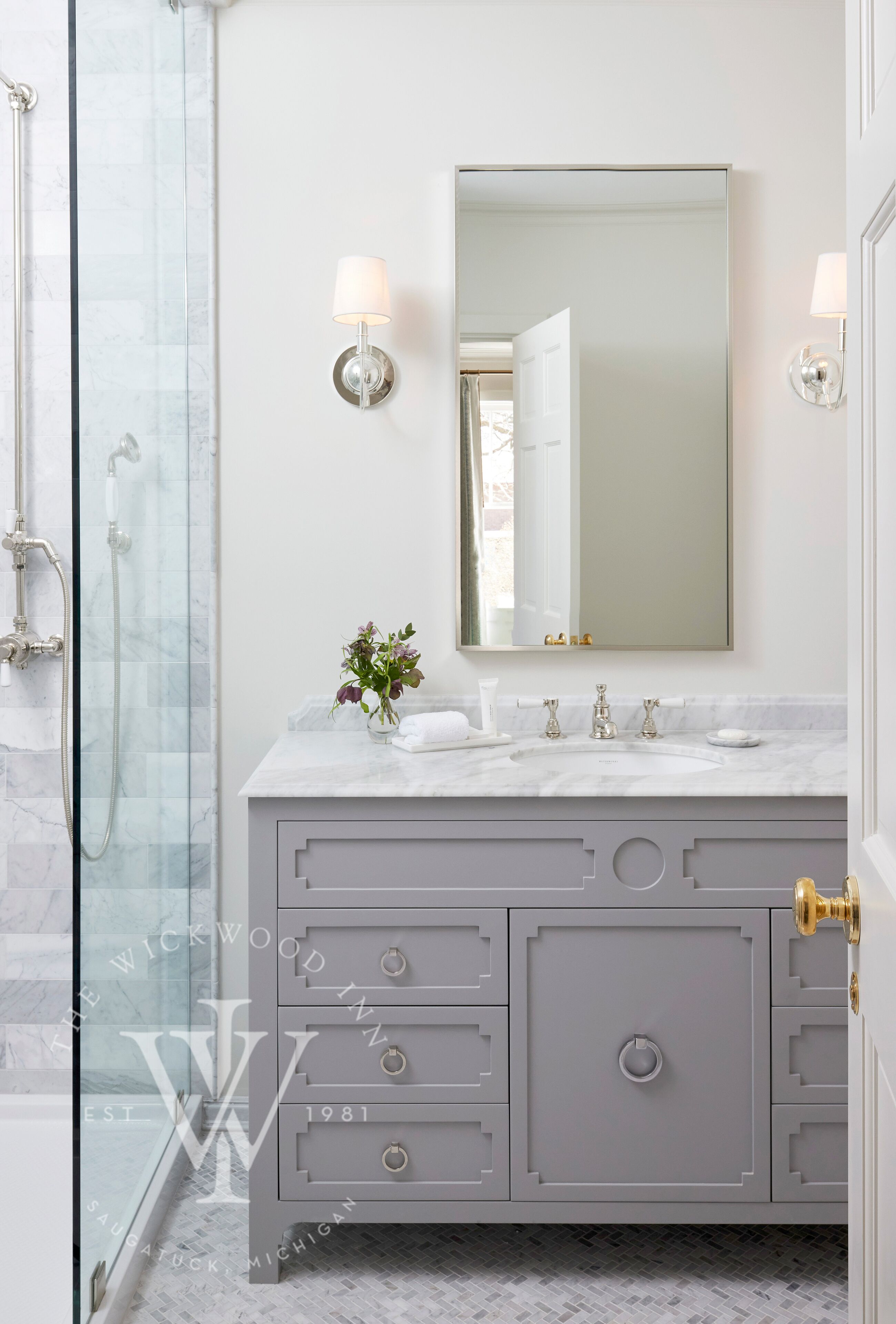 A bathroom with a glass shower enclosure, a marble sink, and a vanity with drawers and a mirror.