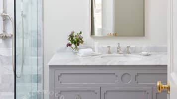 A bathroom with a glass shower enclosure, a marble sink, and a vanity with drawers and a mirror.