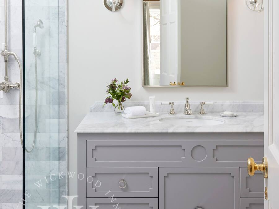 A bathroom with a glass shower enclosure, a marble sink, and a vanity with drawers and a mirror.