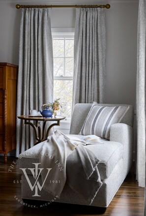 A cozy room with a grey upholstered sofa, a small side table with a vase and teapot, and a window with curtains.