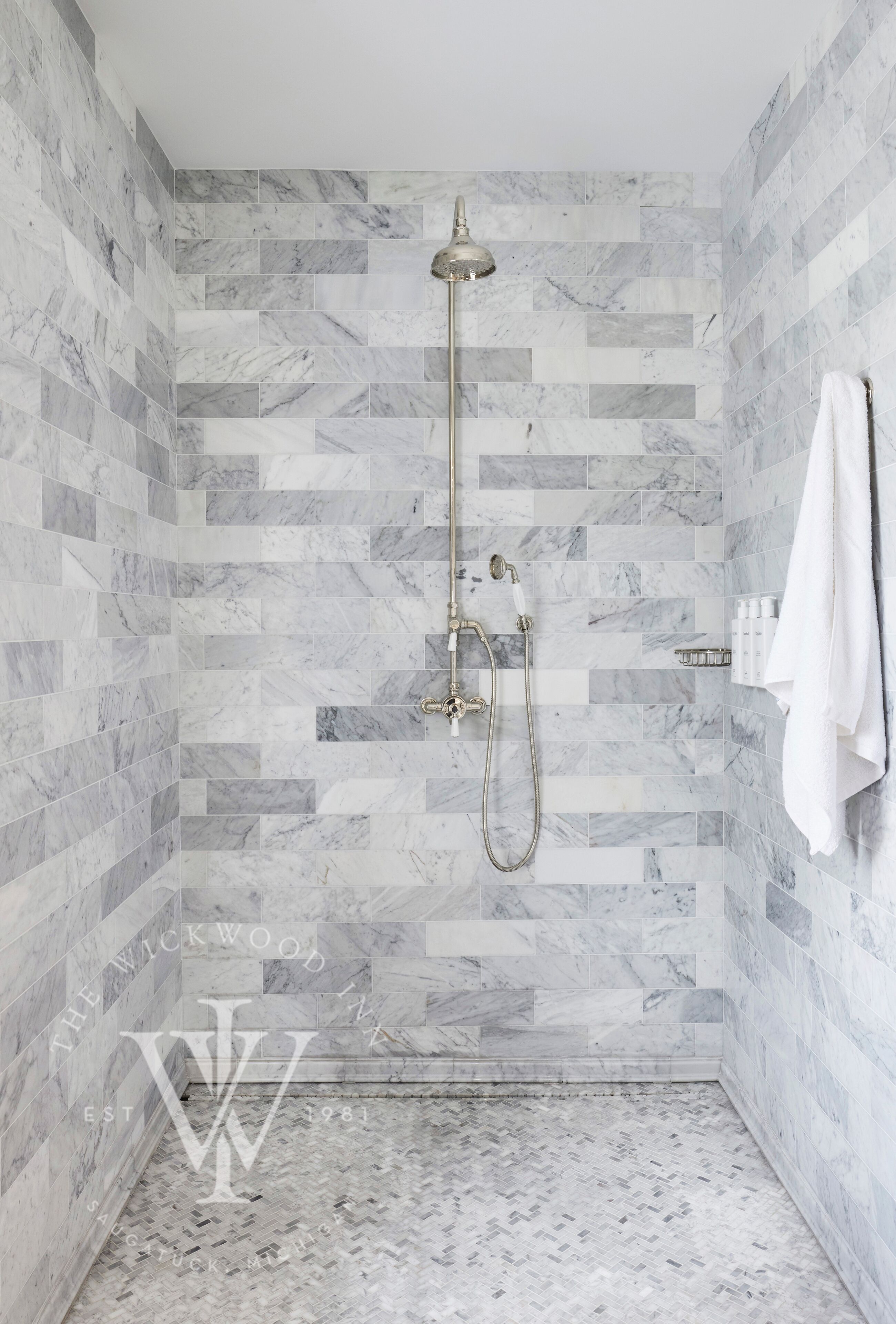 A shower with a handheld showerhead and a wall-mounted faucet, tiled with a marble pattern.