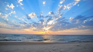 Ein Strand mit blauem Himmel und Sonnenlicht, das sich auf dem Wasser spiegelt.