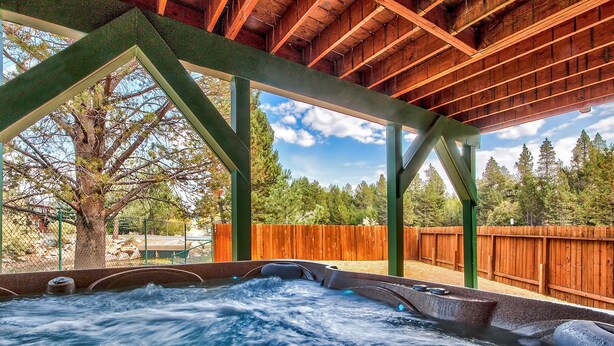 Een hottub onder een houten pergola met uitzicht op een boom en een houten hek.