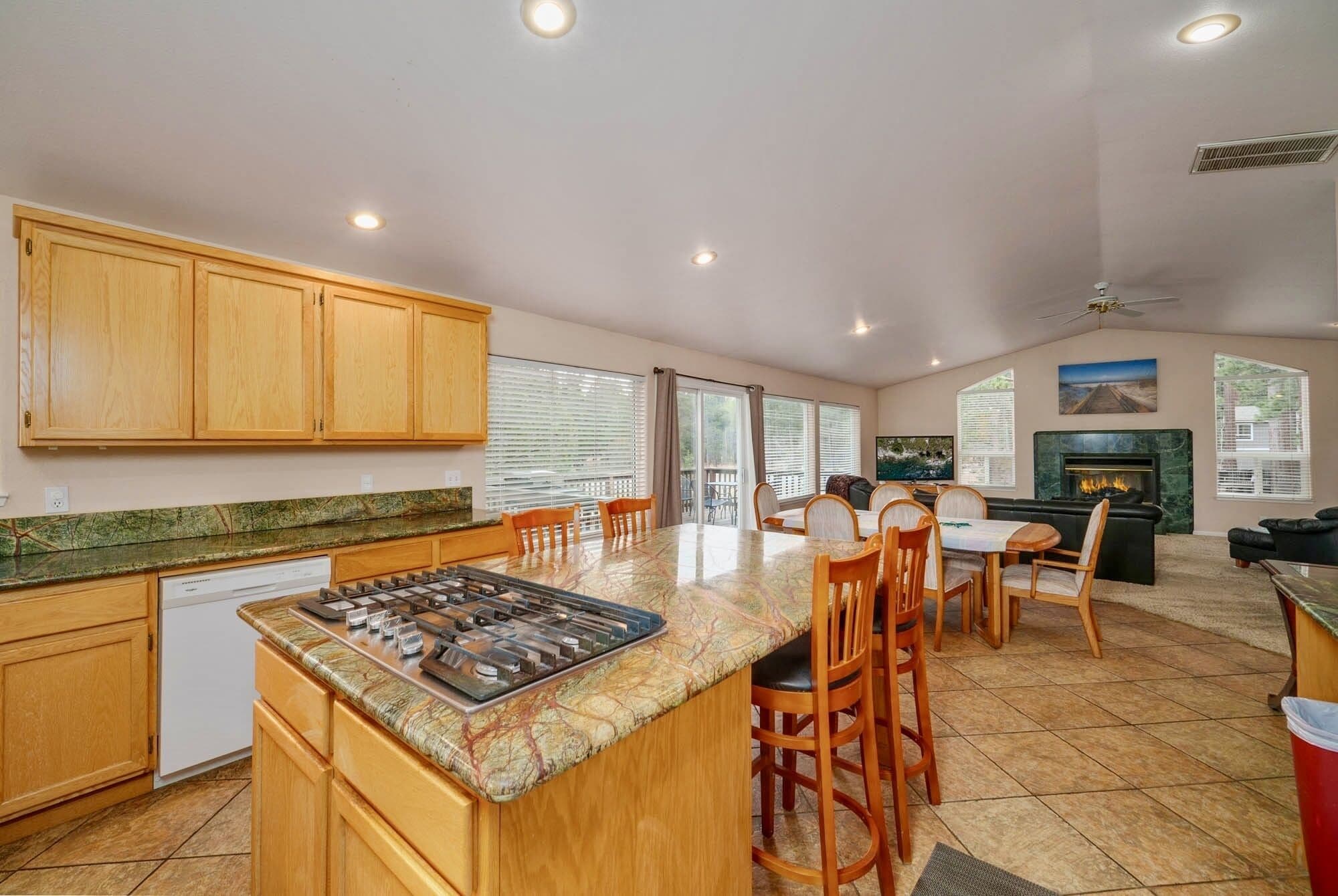 A kitchen with wooden cabinets, a central island with a stove, and a dining area with chairs and a table.