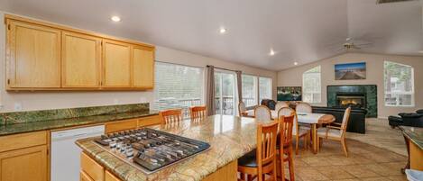 A kitchen with wooden cabinets, a central island with a stove, and a dining area with chairs and a table.