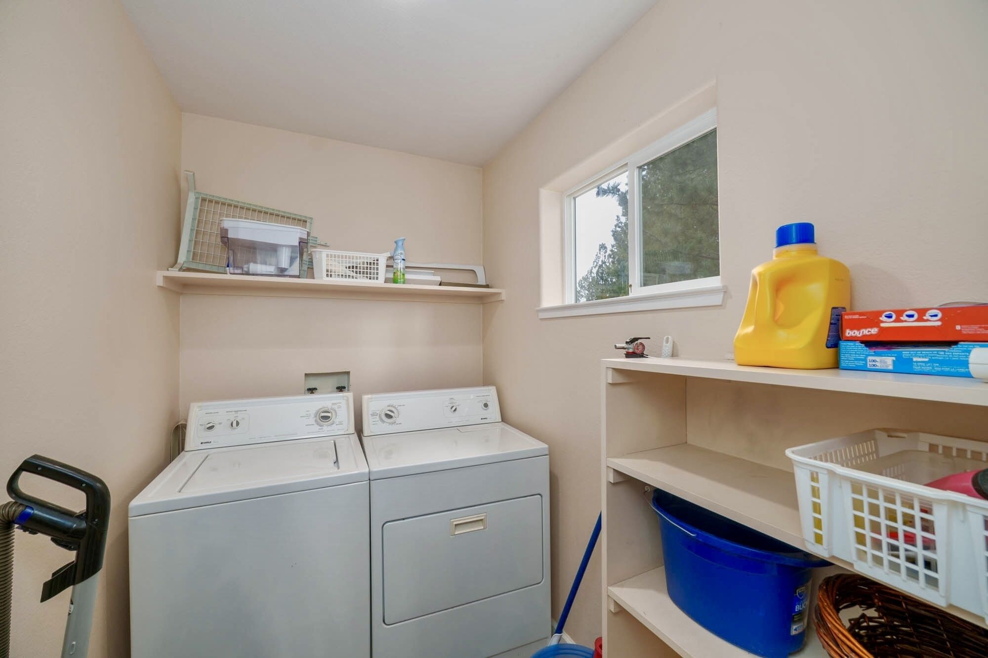 A laundry room with a front-loading washer and dryer, shelves with cleaning supplies, and a window.