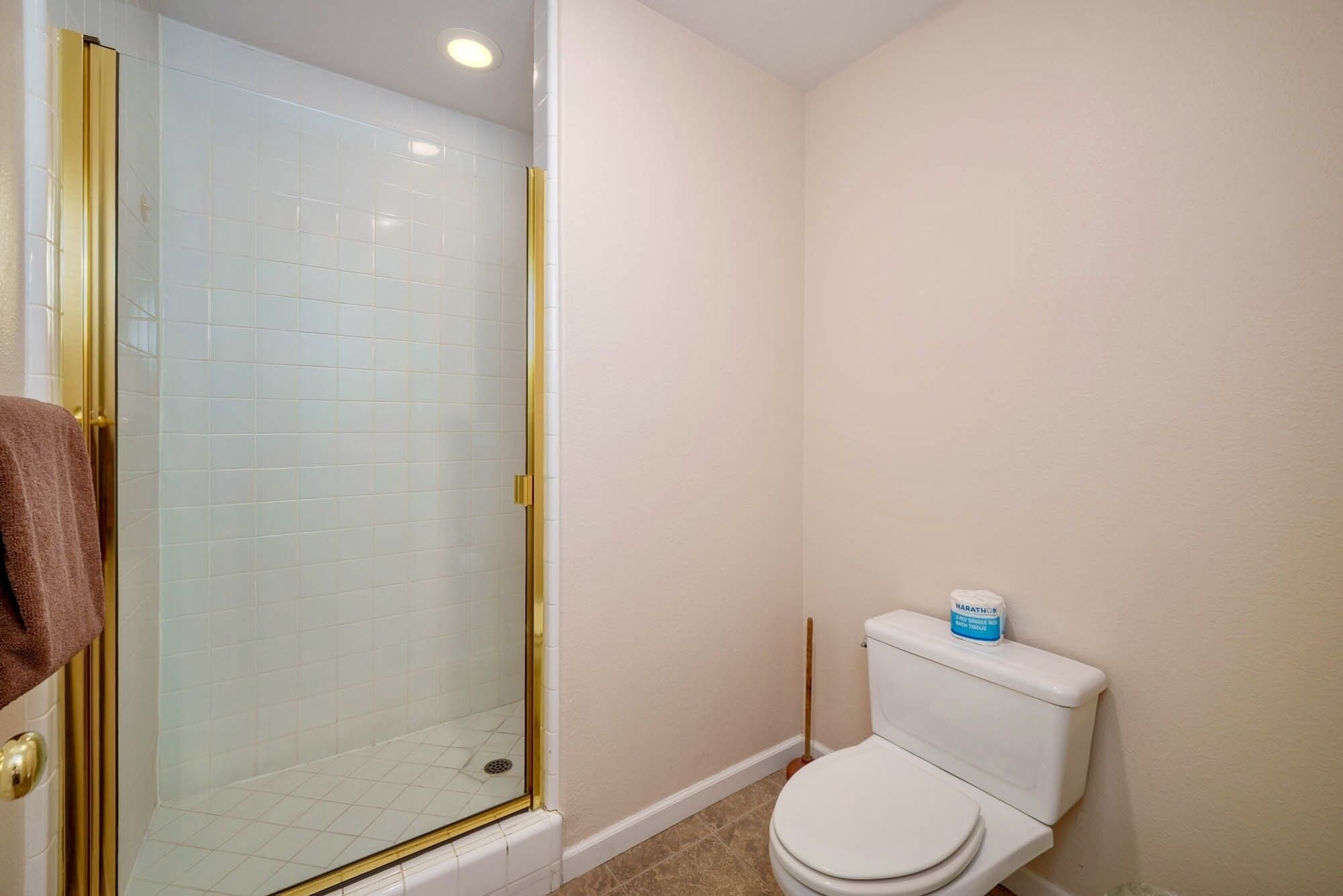 A bathroom with a glass-enclosed shower, a toilet, and a mop on the floor.