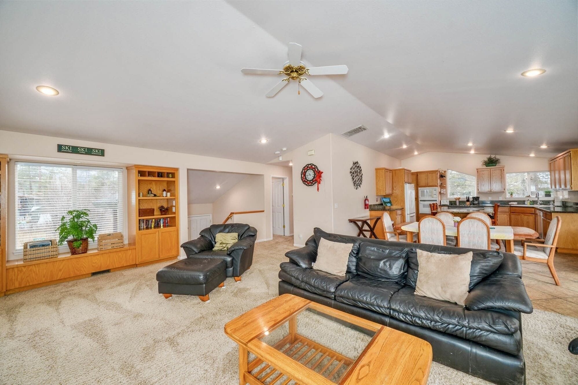 A spacious living area with a black leather sofa, a wooden coffee table, and a ceiling fan.