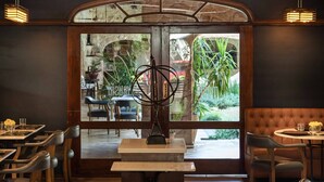 A restaurant interior with a central table, chairs, and a view of an outdoor garden through a large window. - Las Lomas Casa Hotel (Asunción)