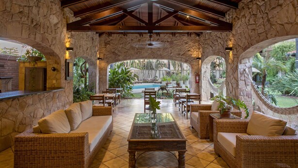 A covered outdoor seating area with stone walls, wicker furniture, and a view of a pool. - Las Lomas Casa Hotel (Asunción)