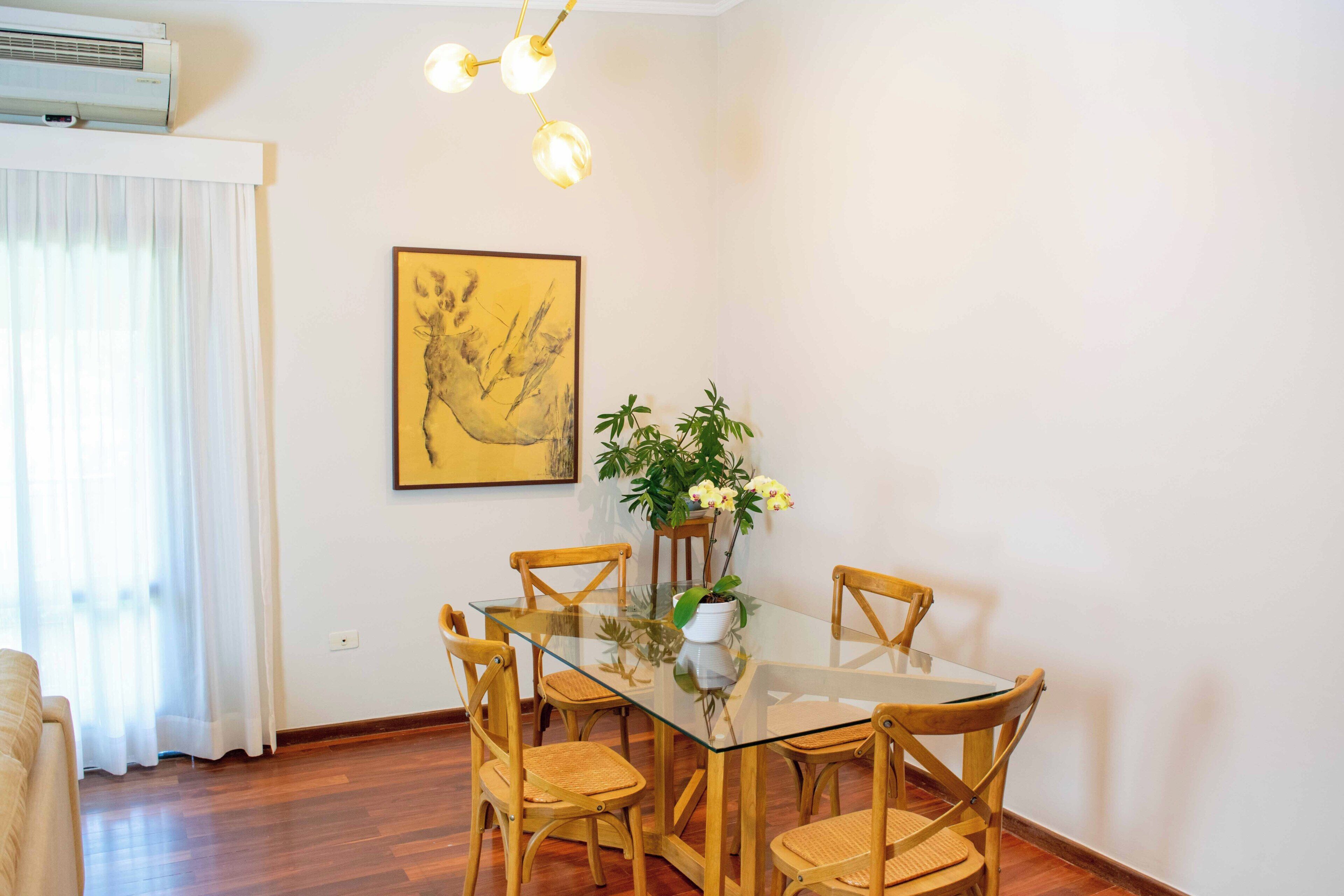 Un coin repas avec une table en verre, des chaises en bois, une plante en pot et une œuvre d’art encadrée accrochée au mur.