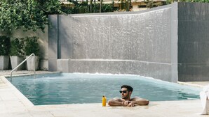 A man relaxing in a swimming pool with a drink beside him. - Las Lomas Casa Hotel (Asunción)