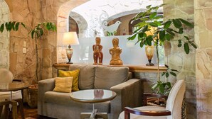 A cozy living area with a stone wall, wooden beams, a sofa, a chair, a small table, and a floor rug. - Las Lomas Casa Hotel (Asunción)