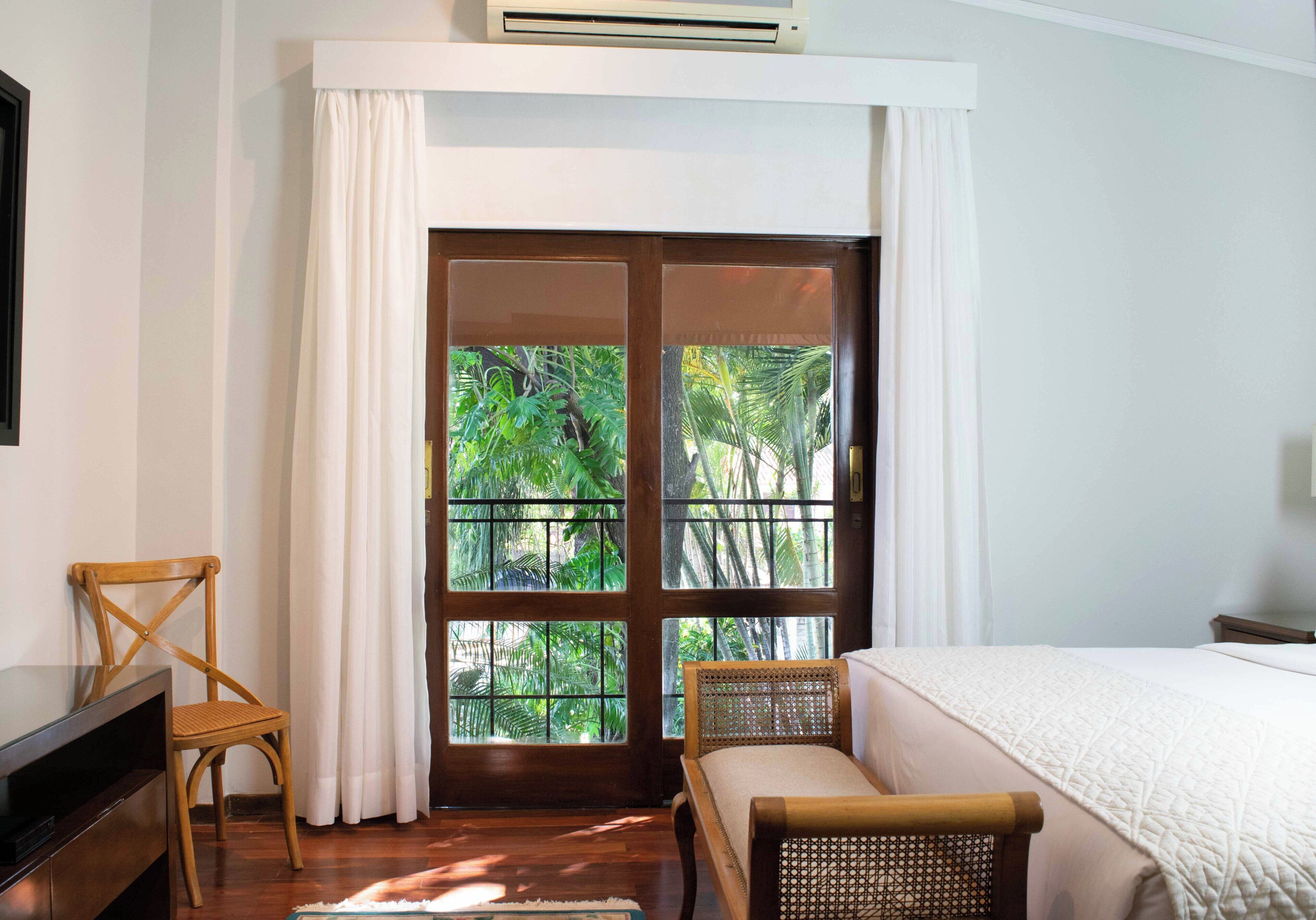 A room with a bed, a chair, a TV, and a window with a view of greenery.