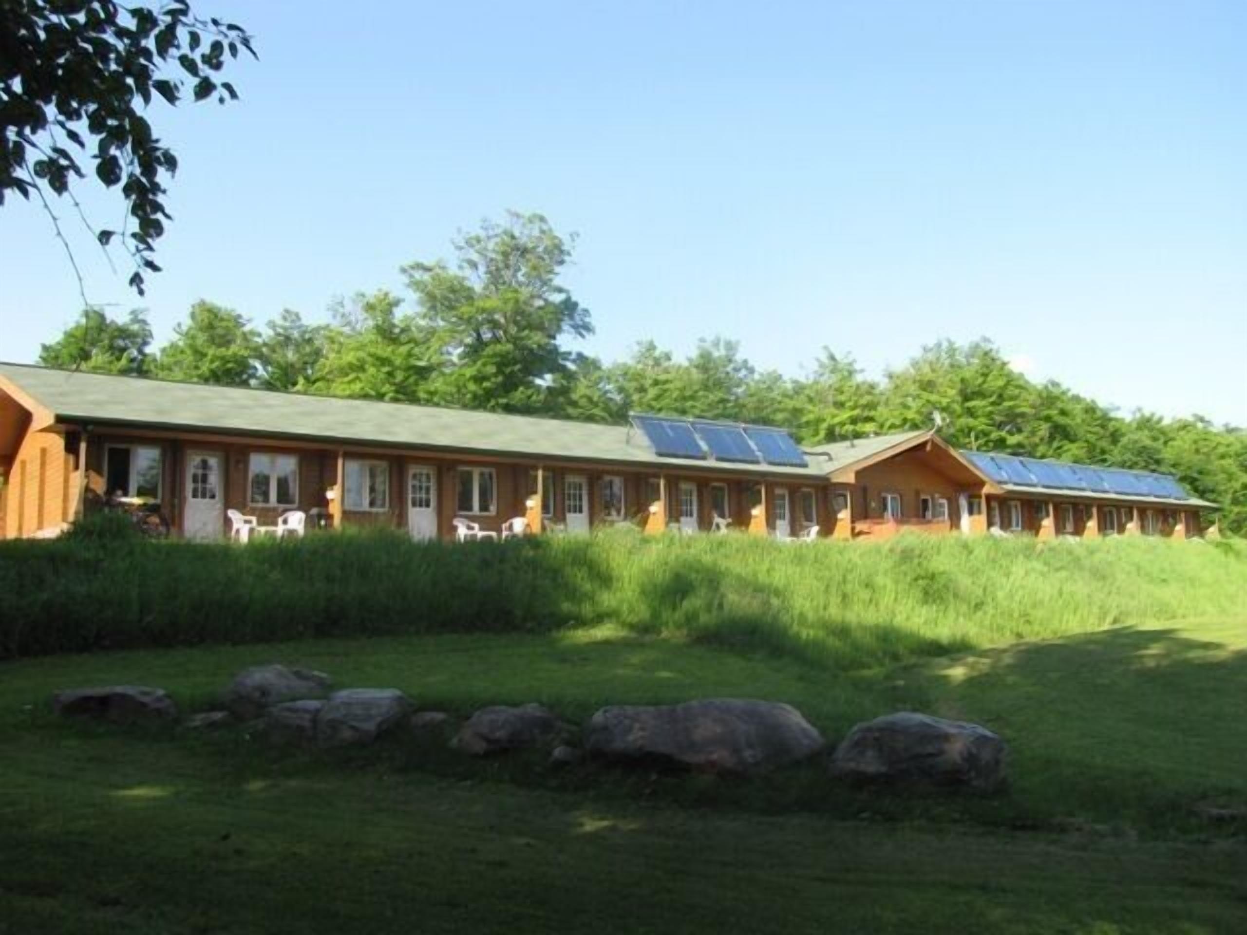 Une rangée de cabanes surmontées de panneaux solaires, situées dans une zone herbeuse avec des arbres en arrière-plan.
