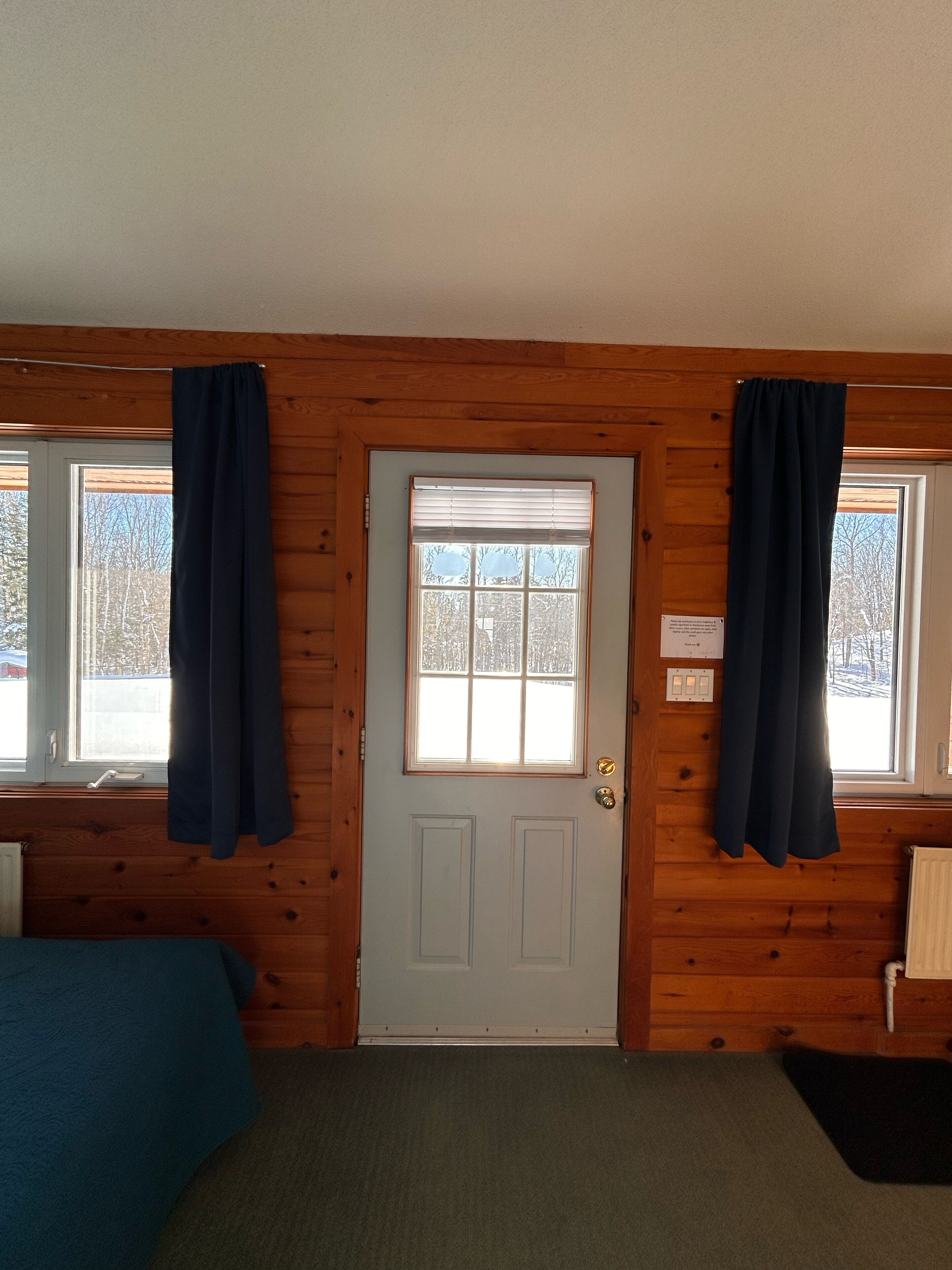 Una habitación con paredes de madera, una puerta blanca con un ventanal y una cama con cubierta azul.