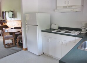 A compact kitchen with a refrigerator, a toaster, a stove, and a coffee maker. There is a small dining table with chairs. - Quiet Bay: Lakeside Escape (Magnetawan)