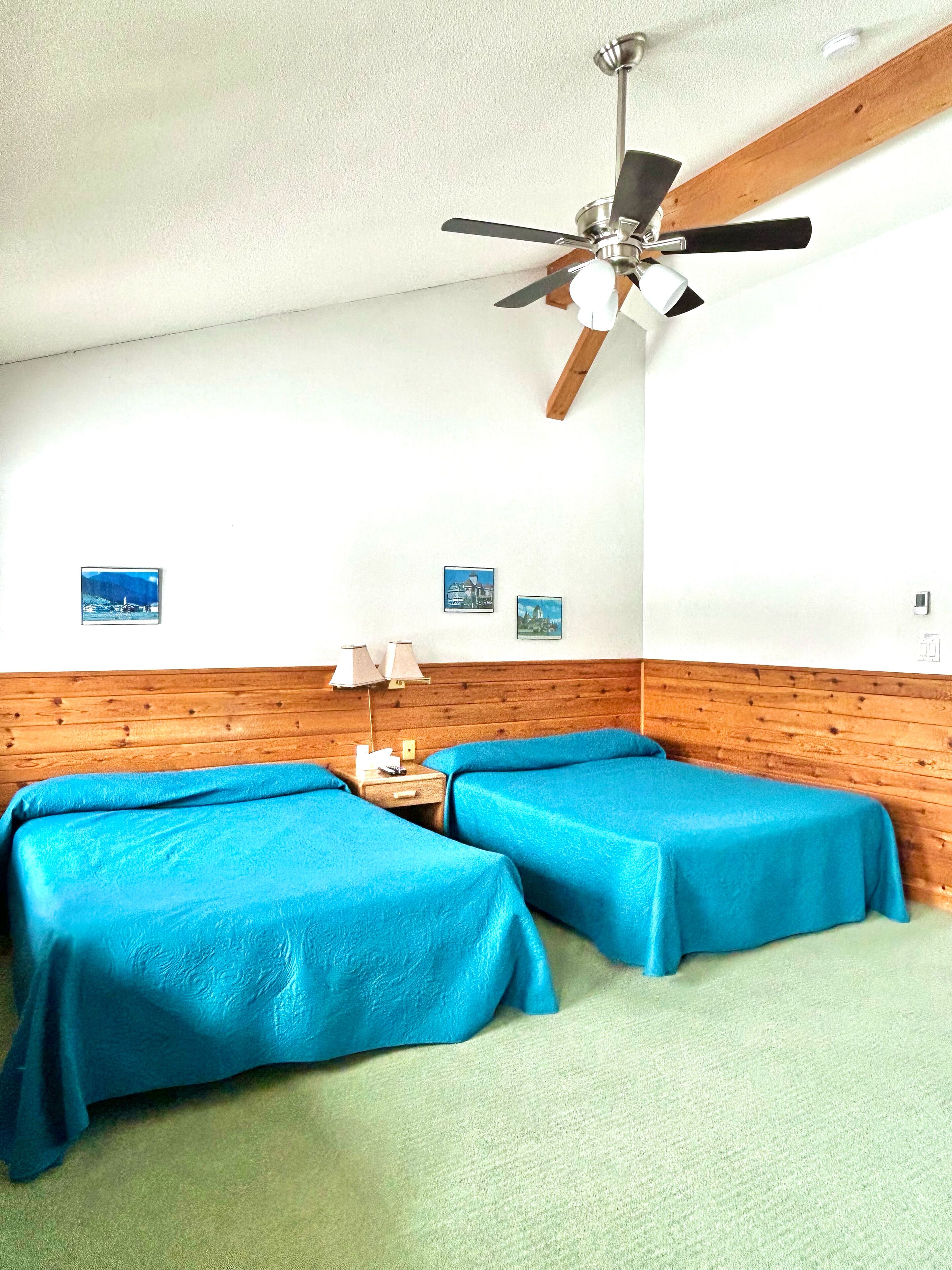 A room with two beds, a ceiling fan, and a wooden headboard.