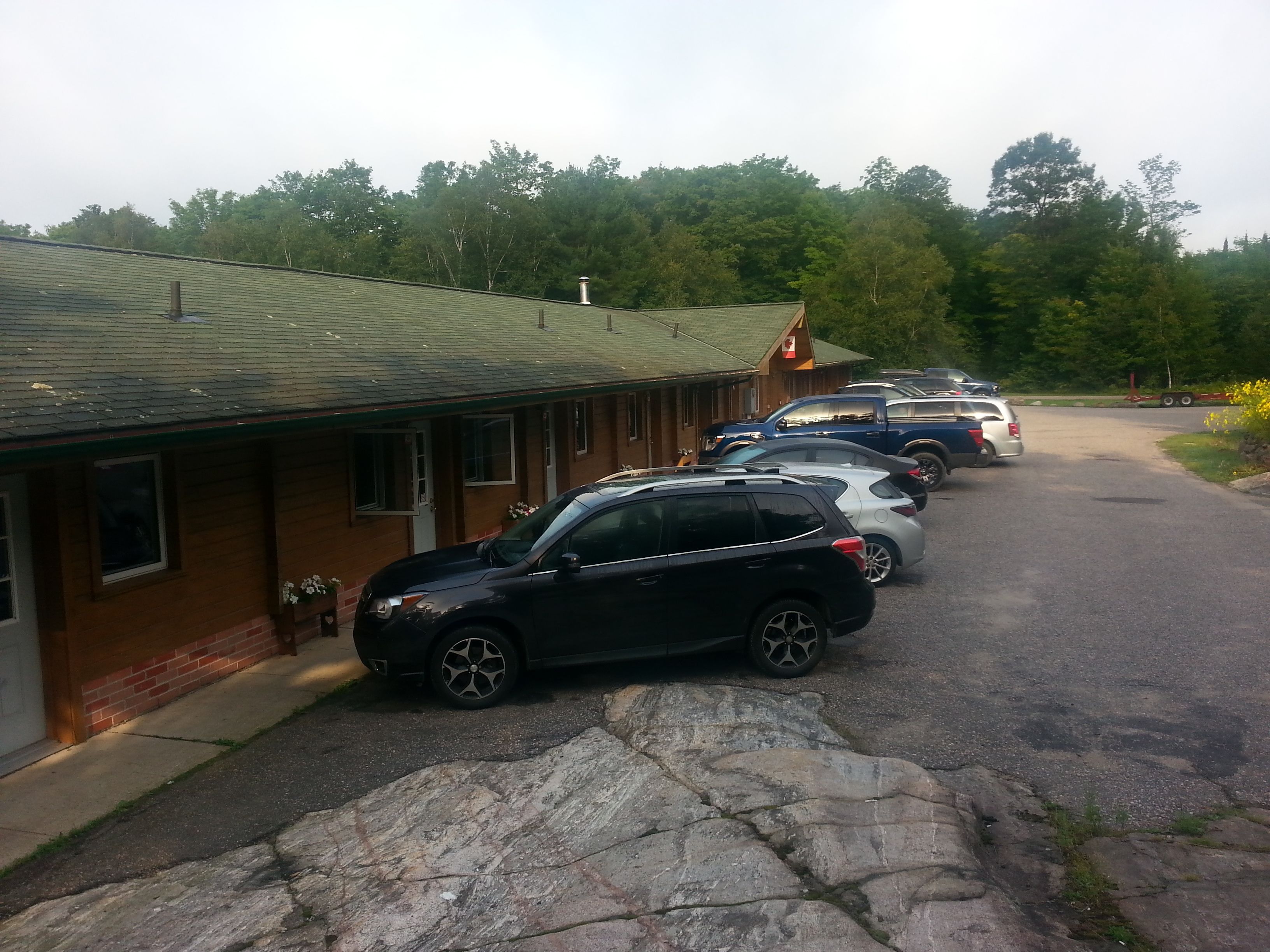 A row of parked cars in front of a building with a green roof and brick walls.