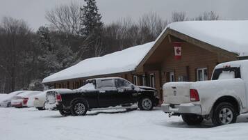 Una cabaña con techo nevado y una bandera canadiense, rodeada de vehículos estacionados.