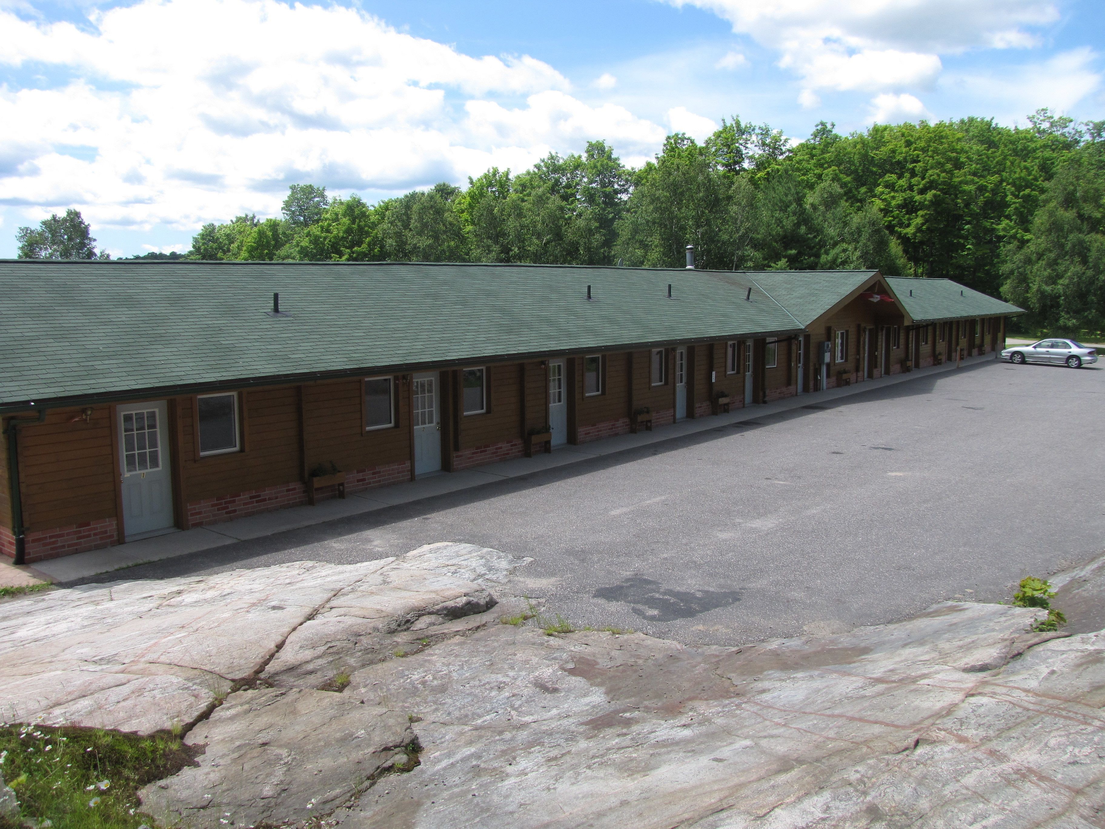 A motel with a green roof, brick facade, and a parking lot.