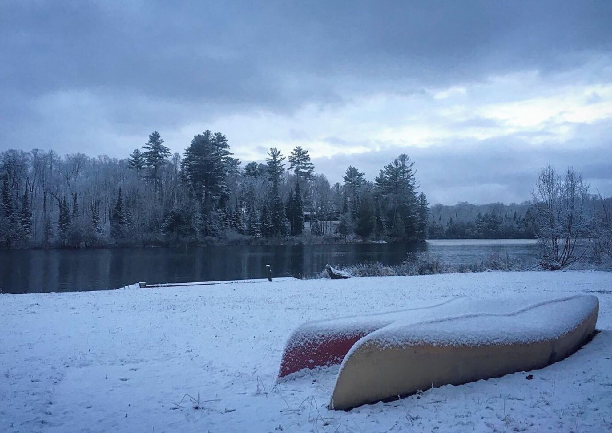 A snow-covered landscape with a lake, trees, and a snow-covered bench.