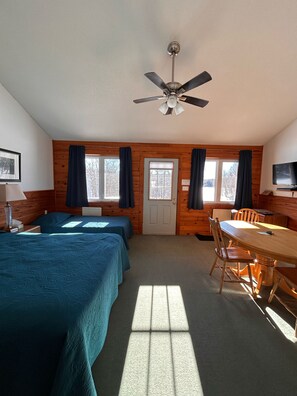 A room with two beds, a dining table, and a ceiling fan. - Quiet Bay: Lakeside Escape (Magnetawan)