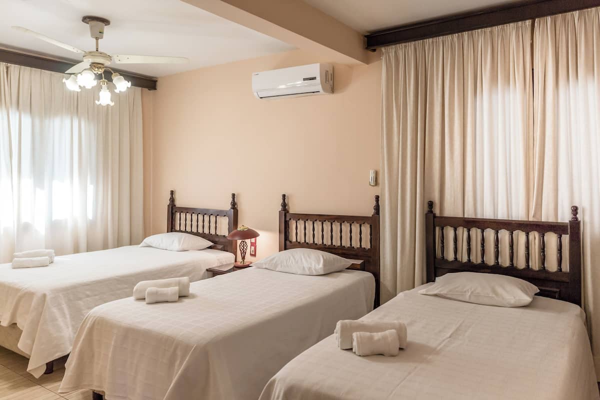 A hotel room with three single beds, a ceiling fan, an air conditioning unit, and a chandelier.