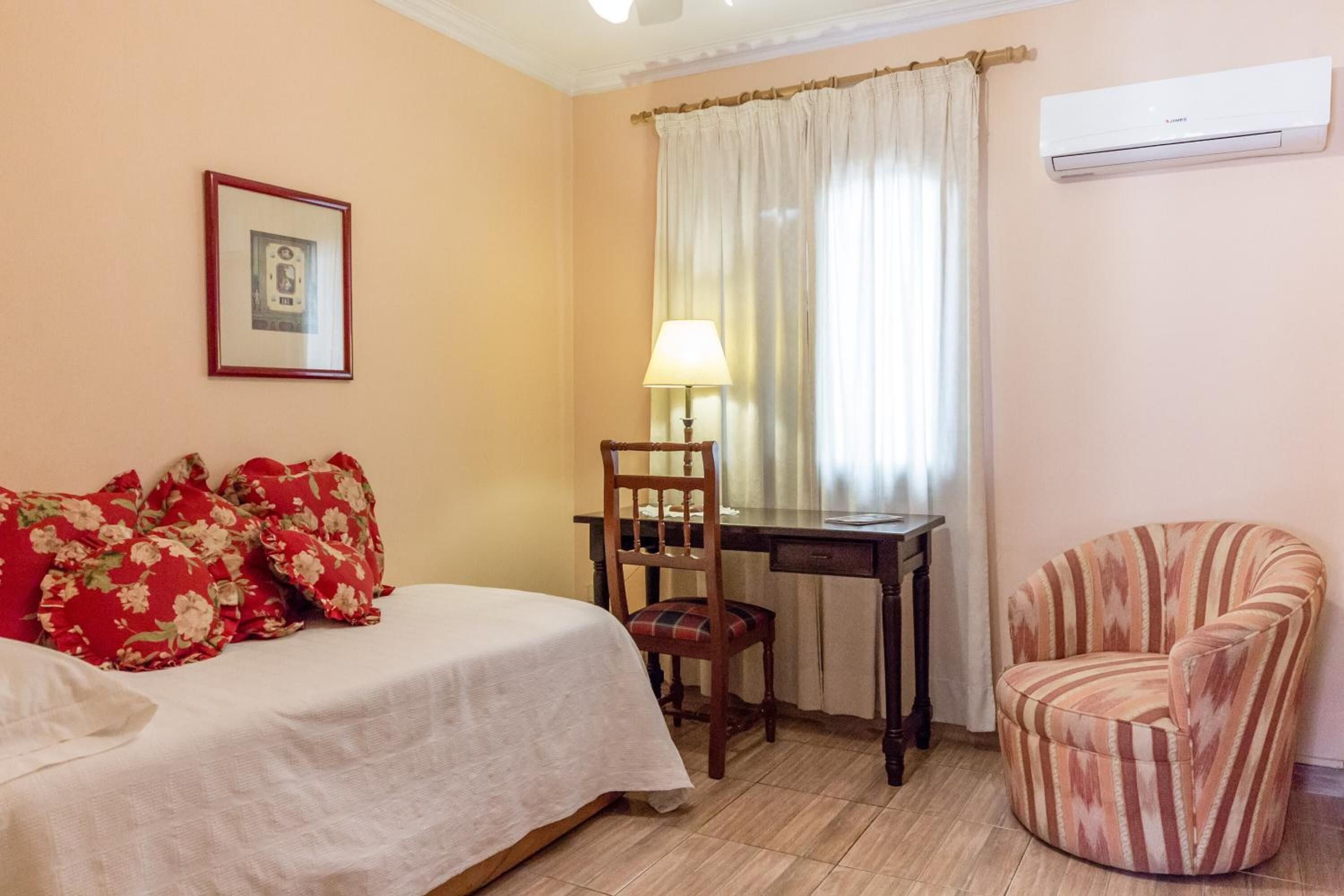 A bedroom with a bed, a desk, a chair, and an air conditioning unit.