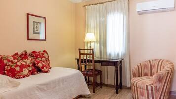 A bedroom with a bed, a desk, a chair, and an air conditioning unit.