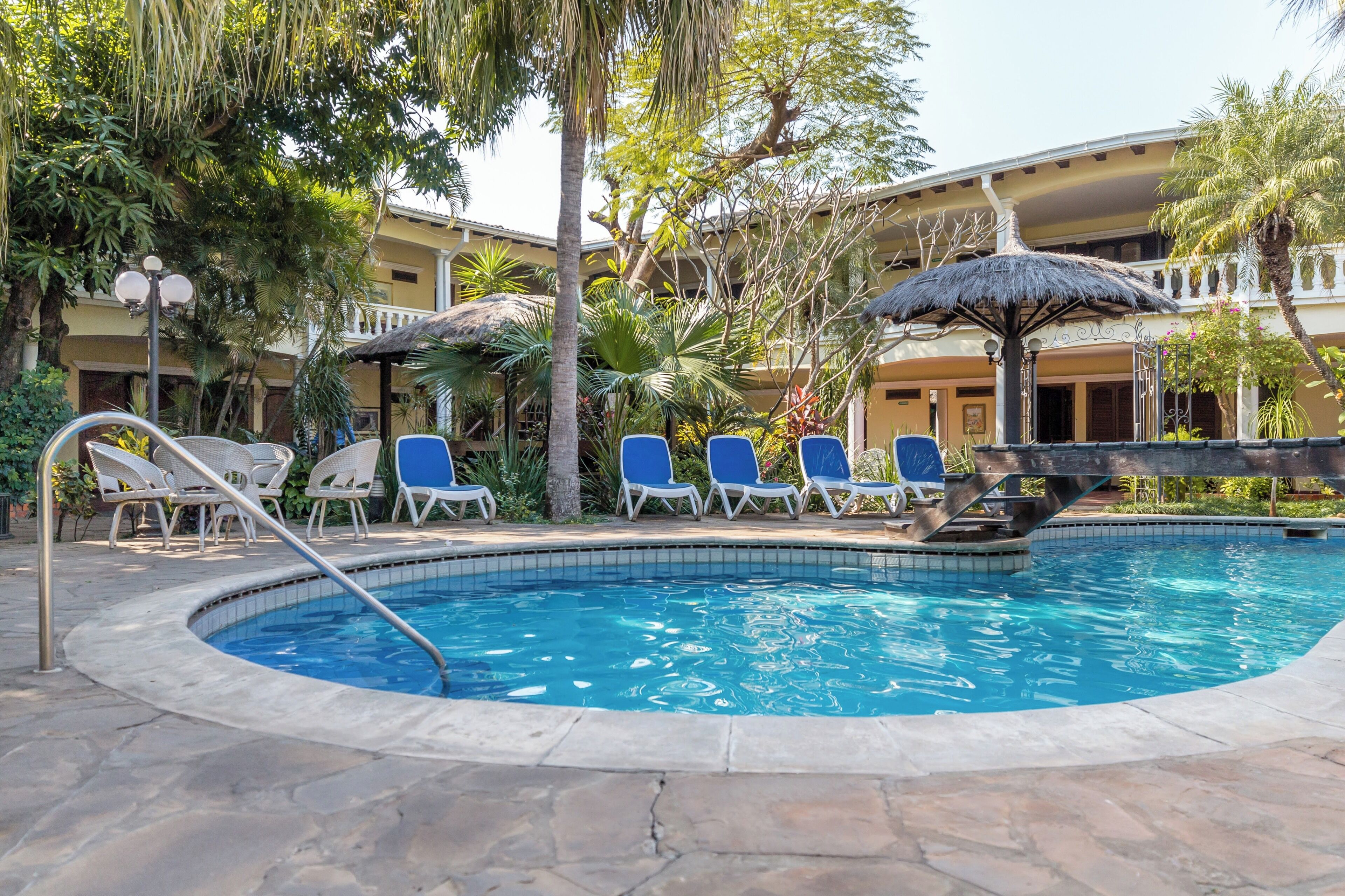 A pool area with lounge chairs, a thatched umbrella, and a building with balconies.