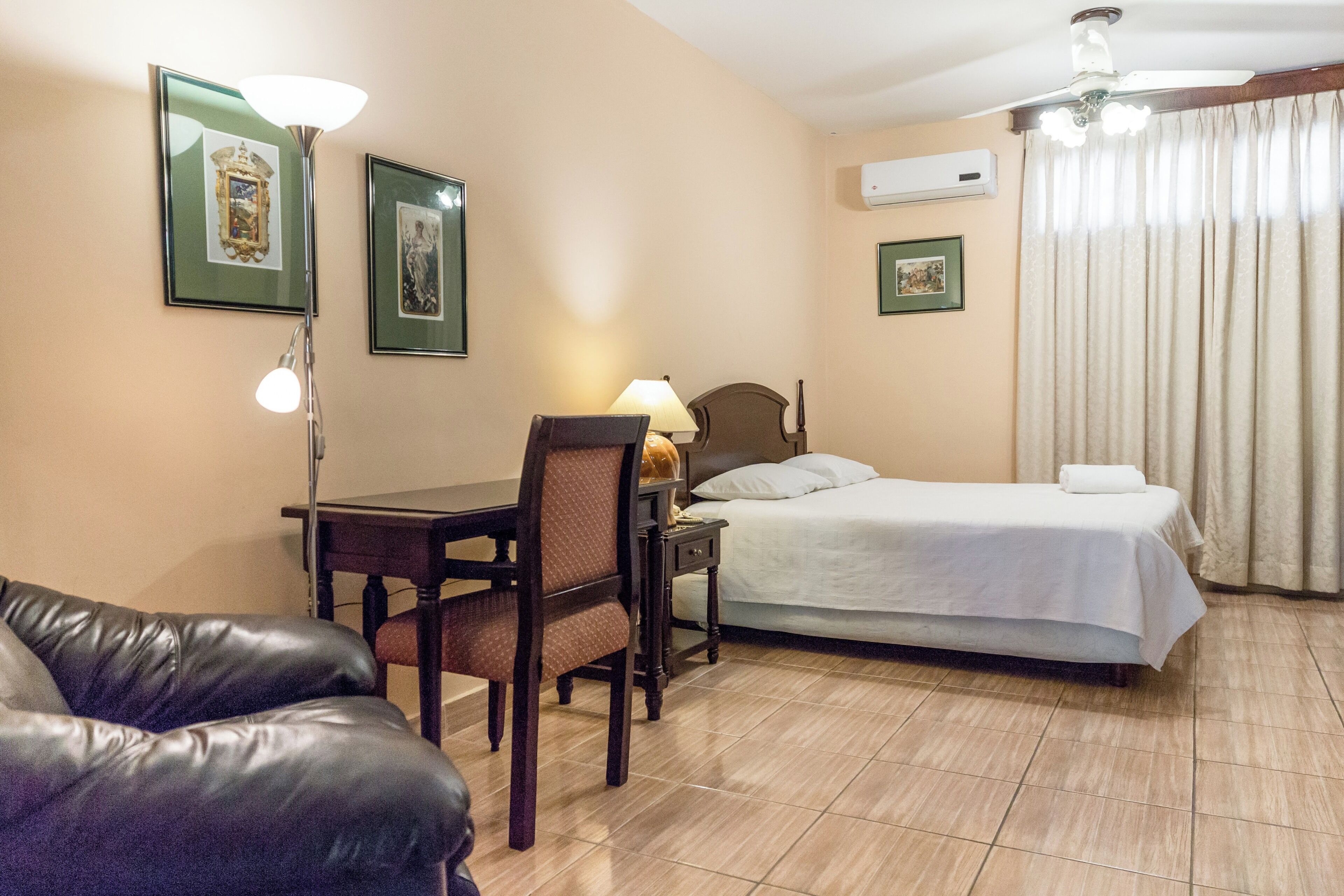 Een hotelkamer met een bed, bureau, stoel, lamp en plafondventilator.
