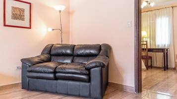A black leather sofa in a room with a tiled floor, a framed picture on the wall, and a lamp.