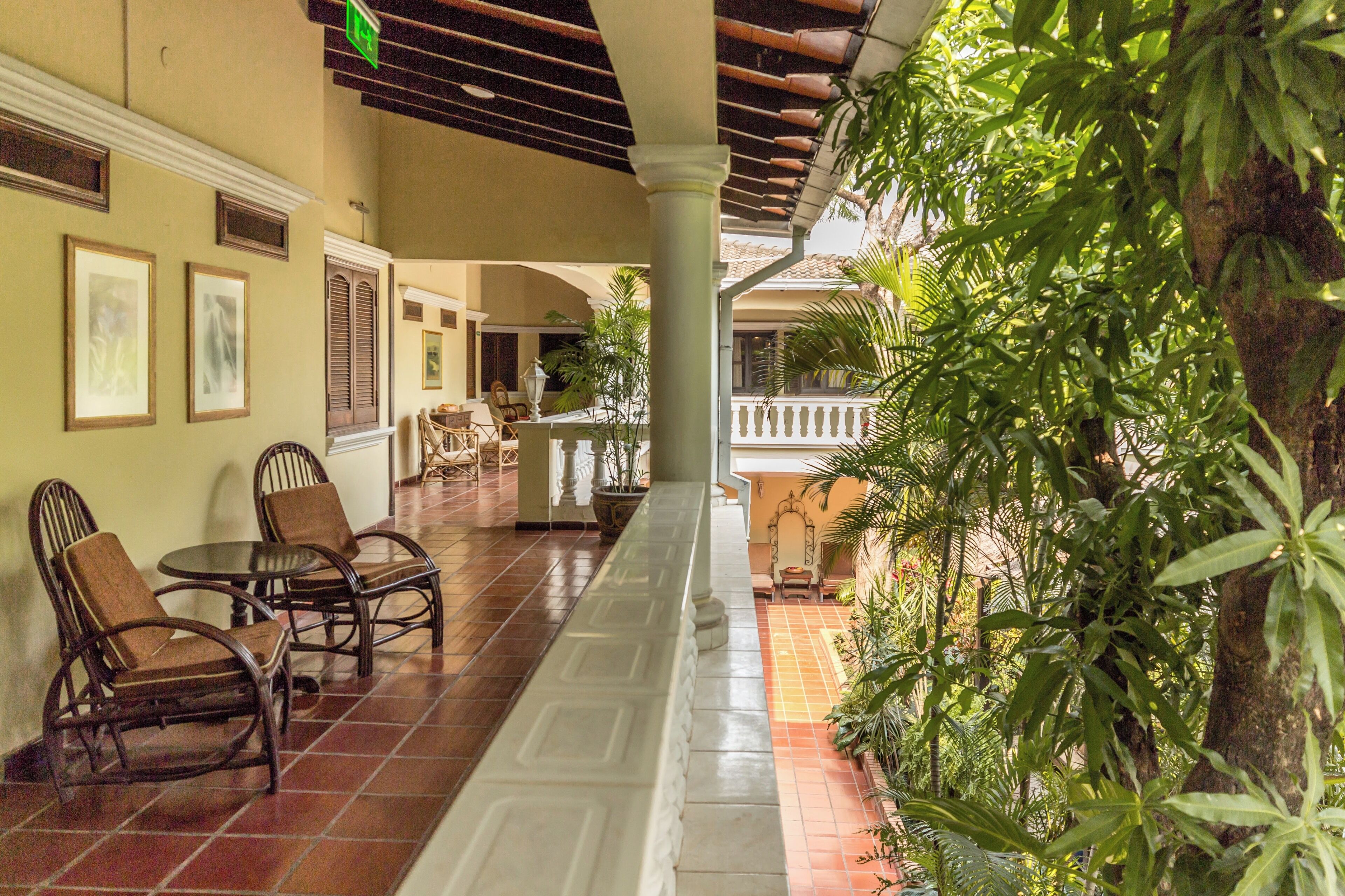 A covered outdoor area with a tiled floor, wooden chairs, a table, and a railing overlooking a garden.