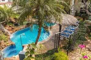 A pool area with a thatched roof, palm trees, and a blue chair.