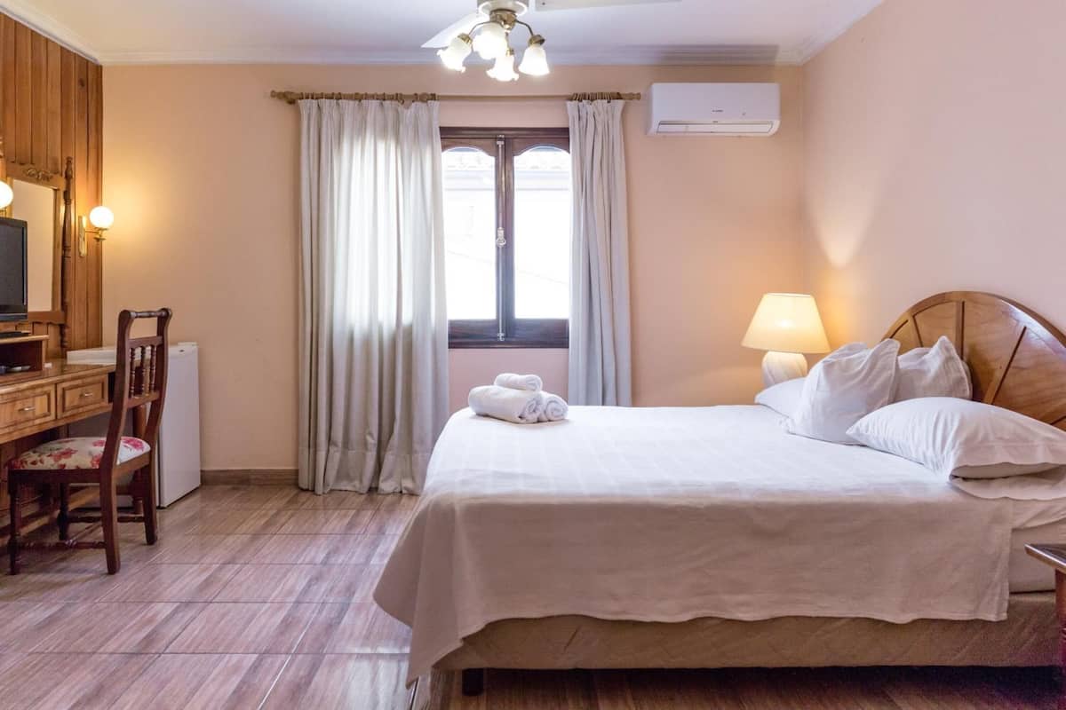 A hotel room with a bed, a desk with a chair, a television, and a window with curtains.