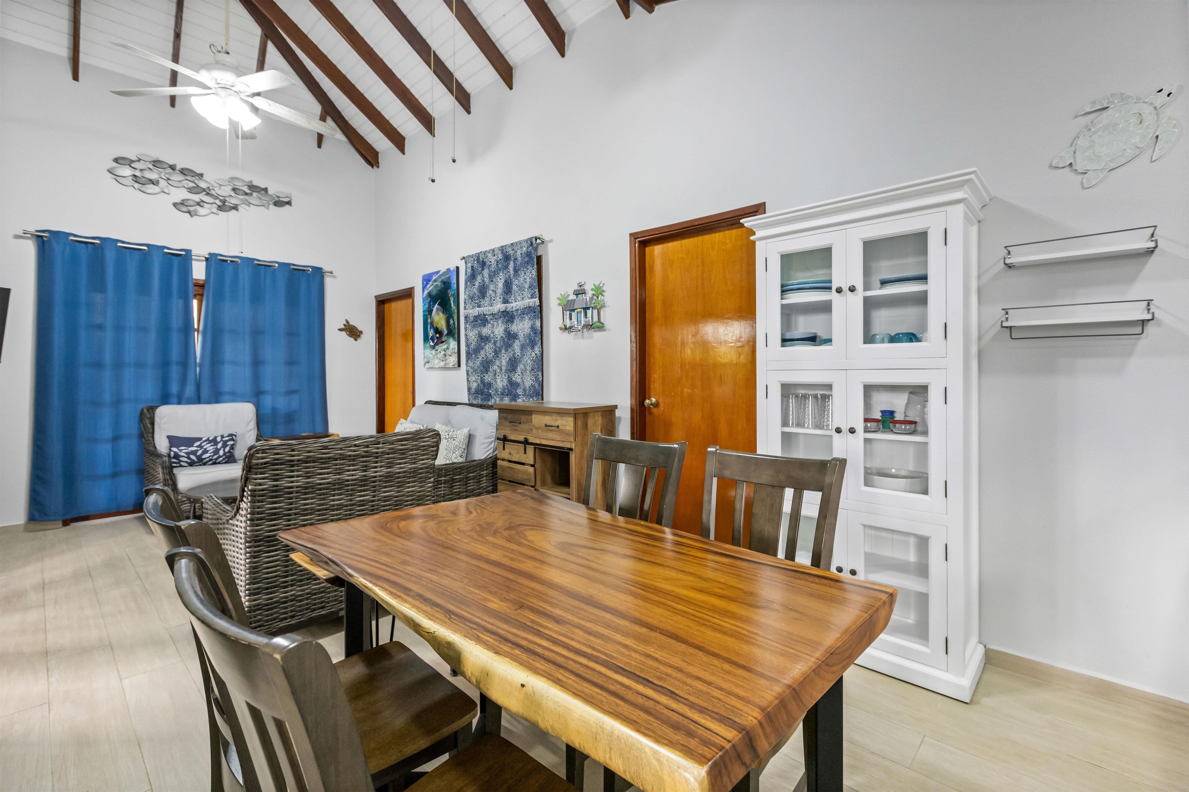 A dining area with a wooden table and chairs, a wicker sofa, and a cabinet with glass doors.