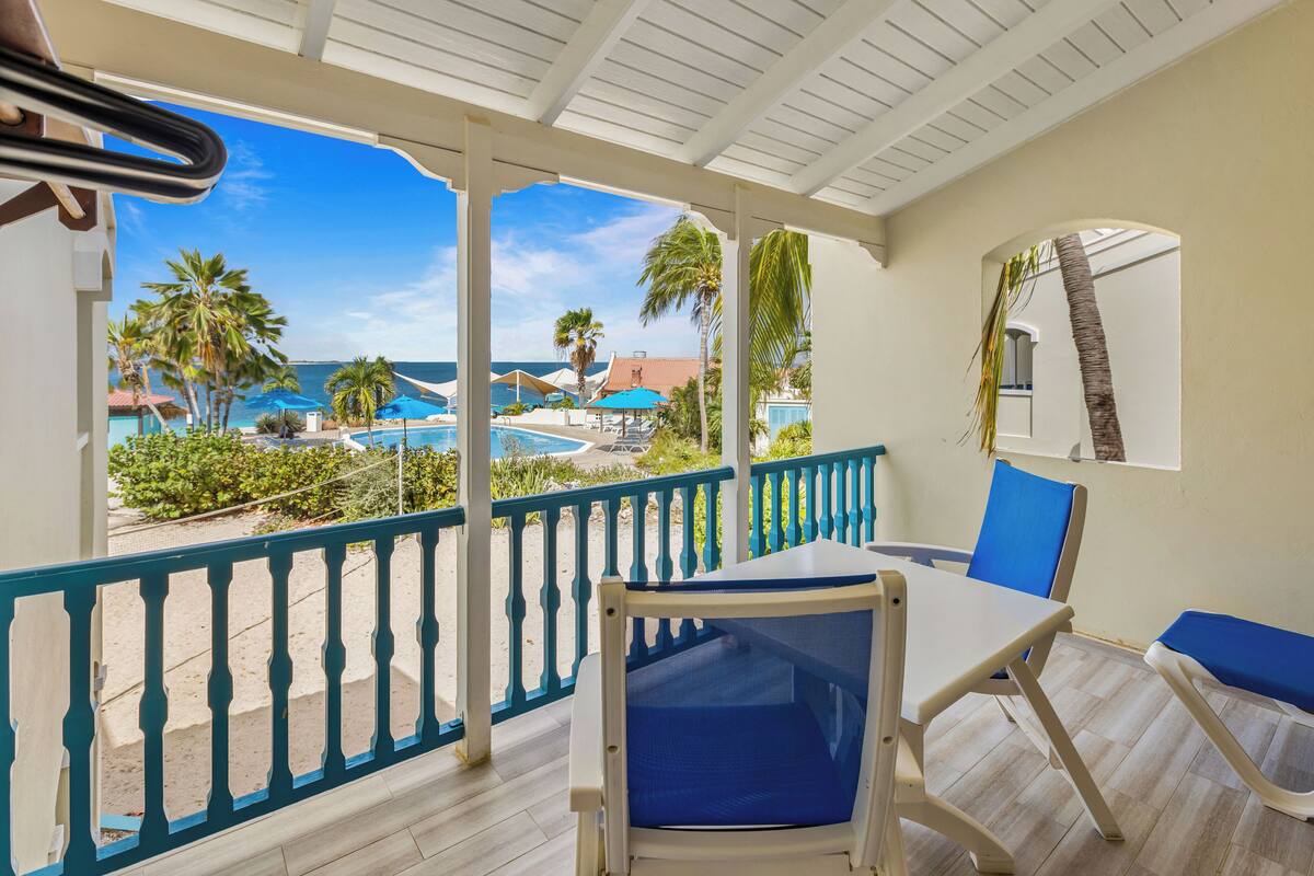 A balcony with a view of a pool, palm trees, and a beach.