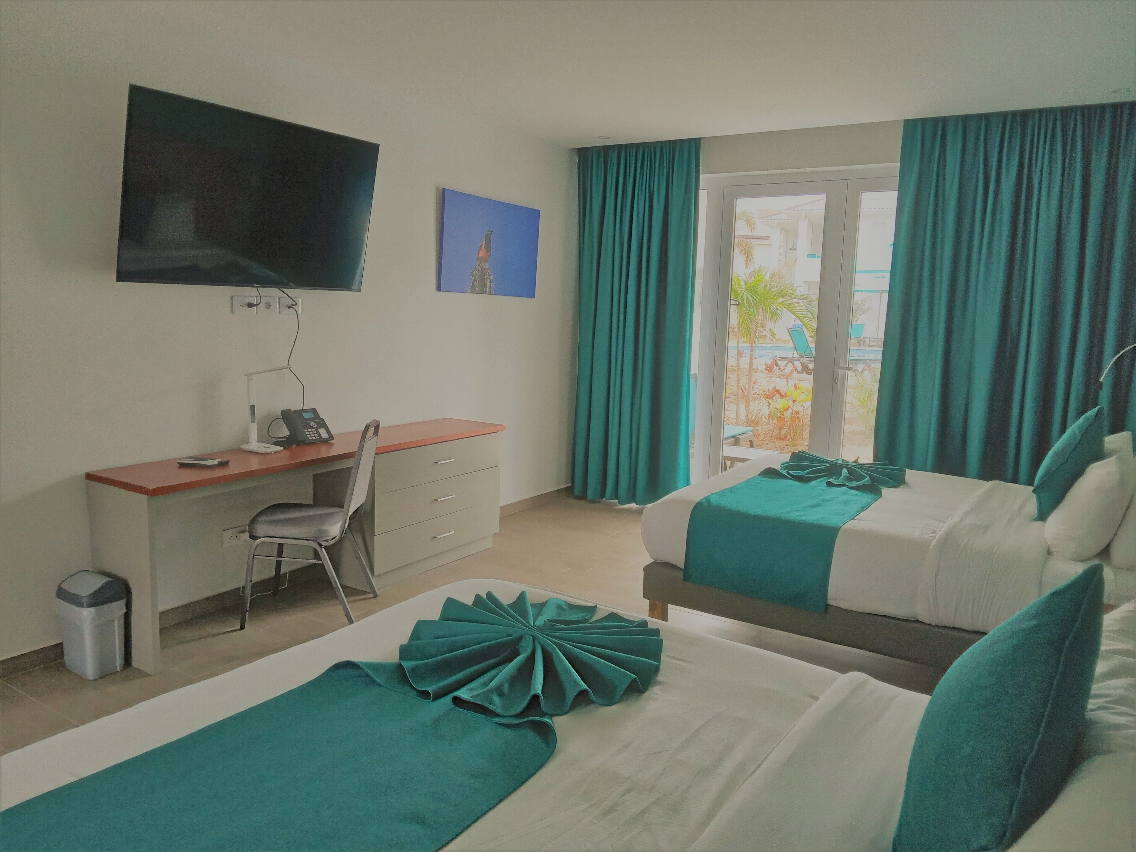 A hotel room with a desk, chair, two beds, a TV, and a window with curtains.