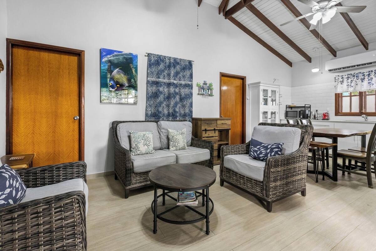 A cozy living area with wicker furniture, a round coffee table, and a kitchen area with a dining table and chairs.