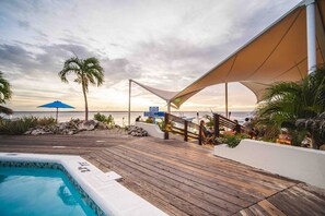 A wooden deck with a pool, palm trees, and a beach view. - Habitat Bonaire (Kralendijk)