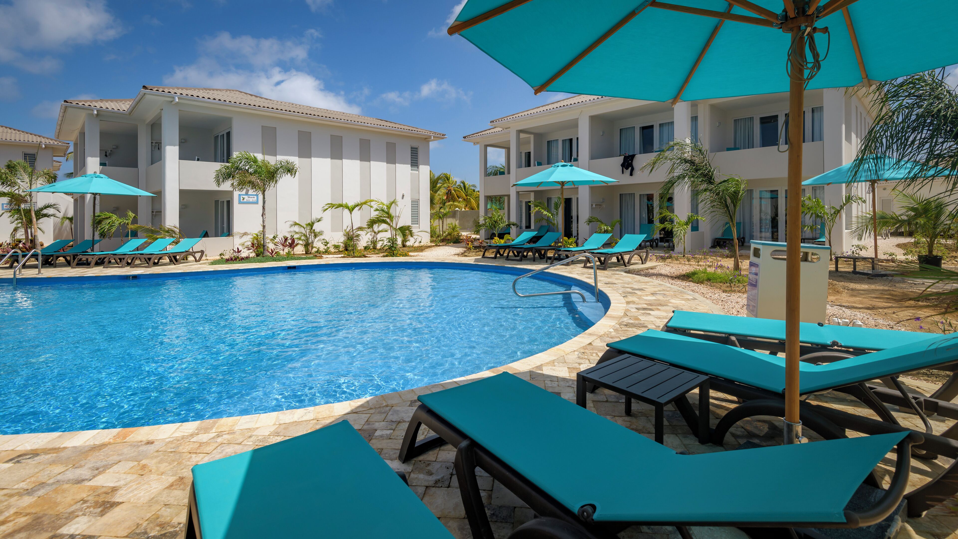 A swimming pool with lounge chairs and umbrellas, surrounded by buildings with balconies.