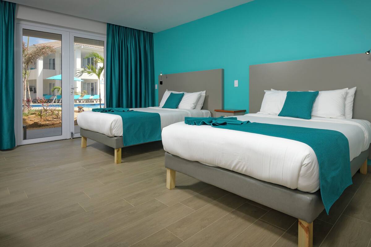 A hotel room with two beds, teal walls, and a view of a pool area.
