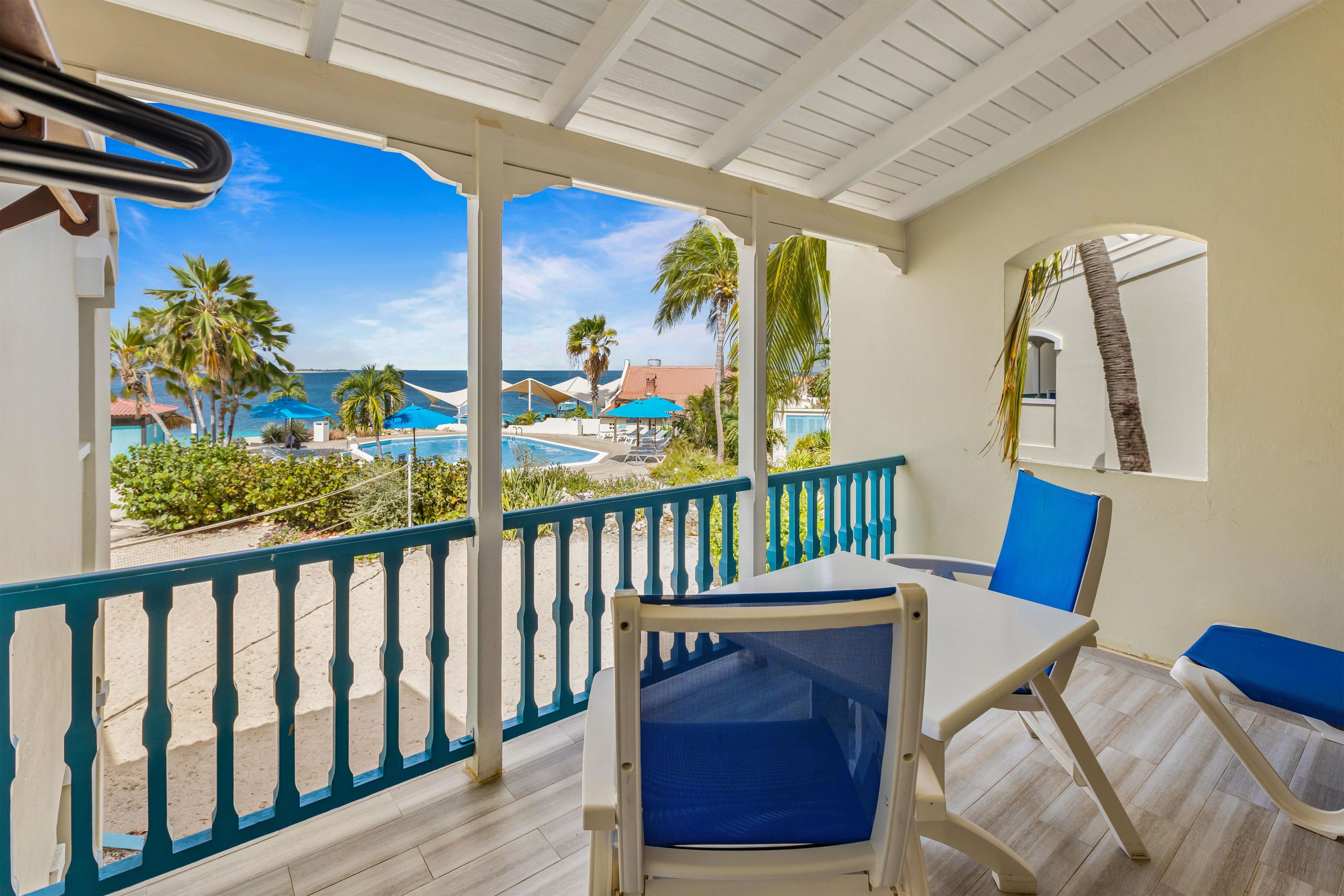 A balcony with a view of a pool and palm trees, a chair, and a table.