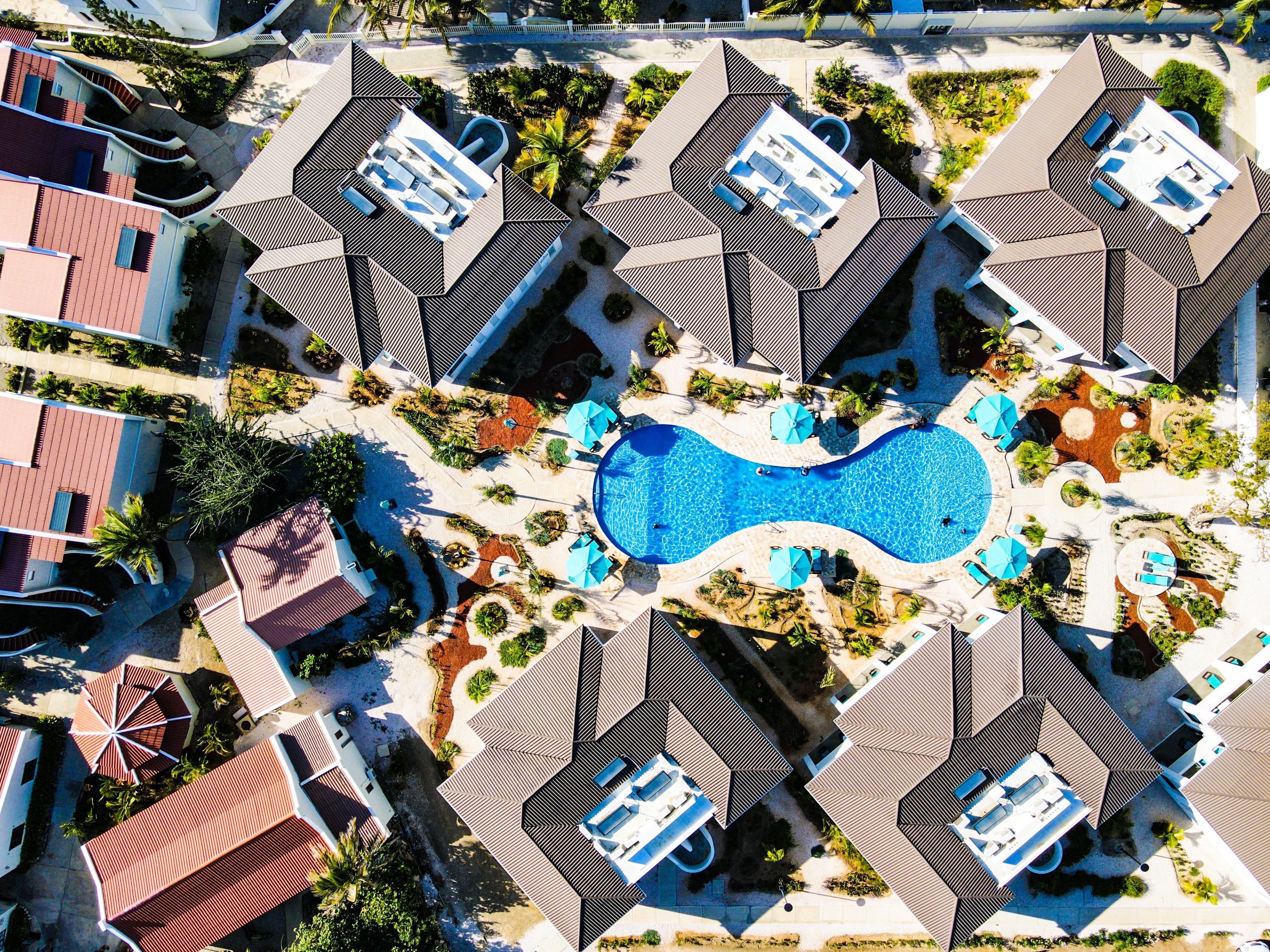 Vista aérea de un complejo turístico con varias construcciones, una piscina central y jardines circundantes.