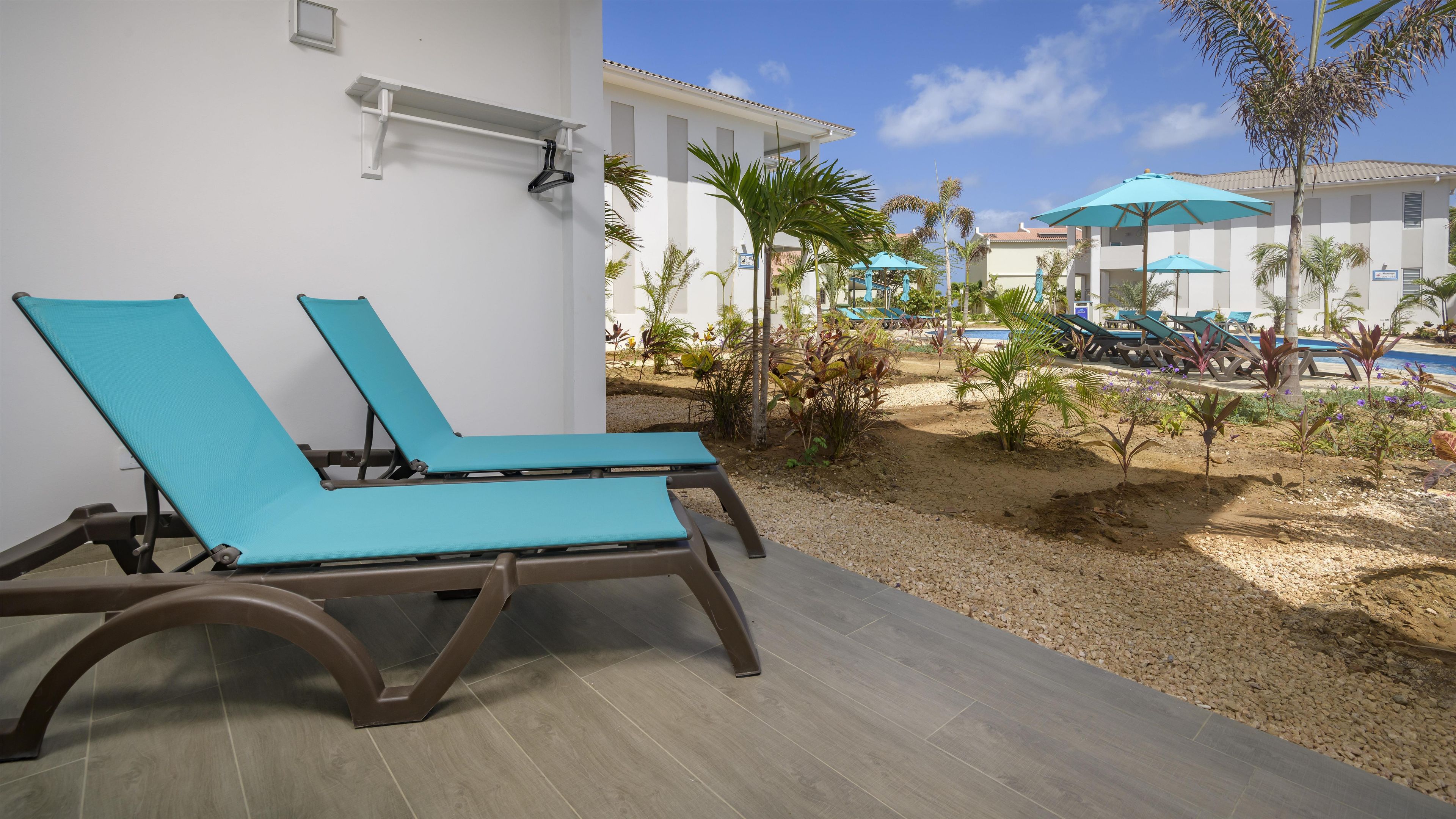 Dos sillones de relax con una piscina y sombrillas al fondo.